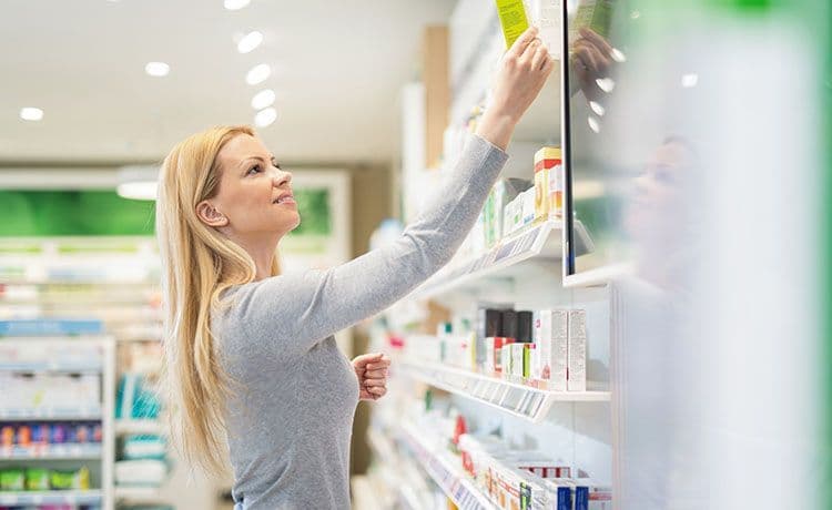 Junge Frau holt eine Packung aus einem Regal in einer Drogerie.