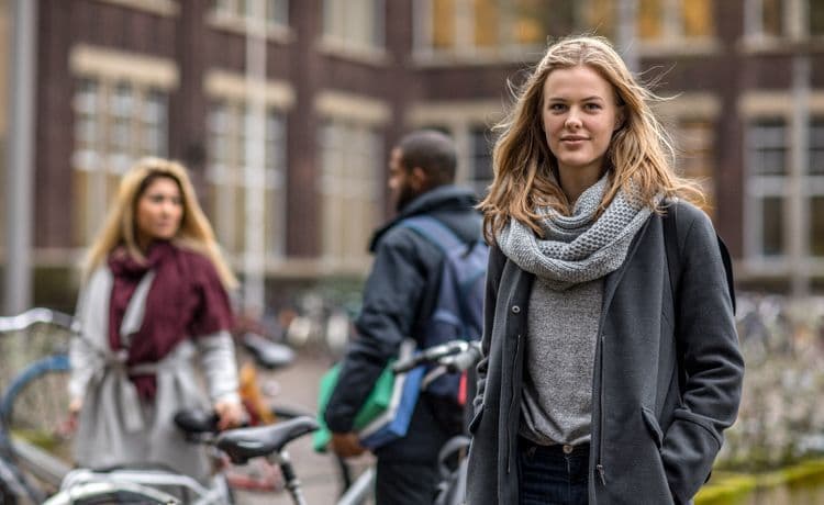 Junge Frau steht vor ihrer Uni.