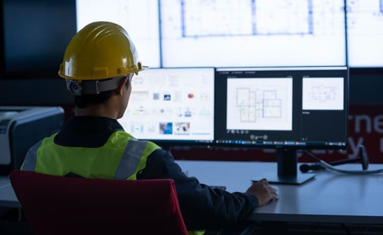 Junger technischer Systemplaner sitzt vor Bildschirm, an dem technische Pläne zu sehen sind.