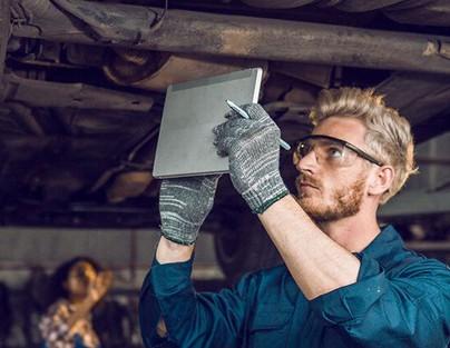 Ein junger Kfz-Mechatroniker mit Tablet in der Hand arbeitet an einem Auto.