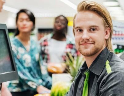 Ein junger Verkäufer sitzt an der Kasse eines Supermarkts.