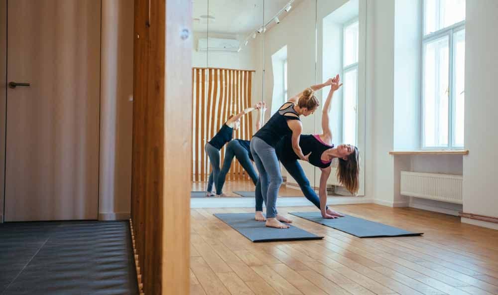 Gymnastiklehrerin hilft einer Schülerin beim Stretching.