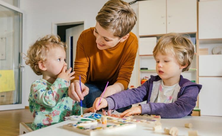 Junge Sozialarbeiterin spricht mit Kindern, die malen.