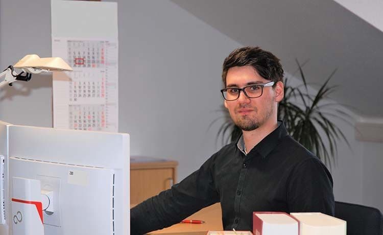 Junger Mann sitzt im Büro am Schreibtisch.