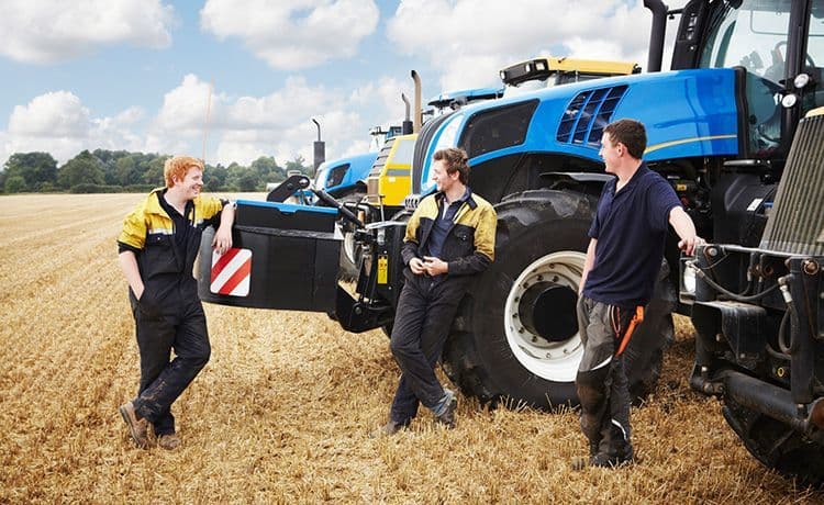 Drei Männer stehen auf einem Feld neben Traktoren.