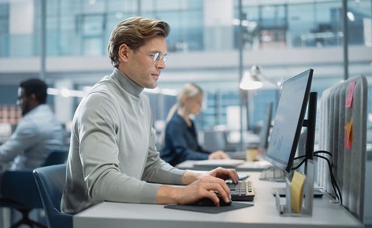 Data Analyst sitzt am PC im Büro und führt eine Datenanalyse durch.