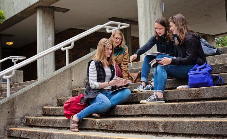 Studierende des dualen Studiums Gesundheitsmanagement sitzen auf einer Treppe und reden miteinander.