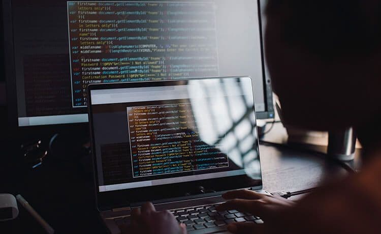 Informatiker sitzt an einem Laptop mit Quellcode und programmiert.