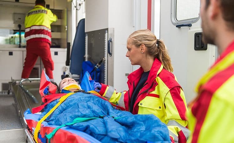 Zwei Rettungsassistenten kümmern sich um den Transport eines Unfallopfers auf einer Trage und schieben ihn in einen Rettungswagen.
