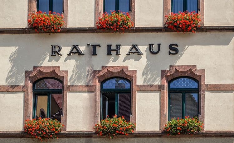 Foto von Rathaus mit schönem Blumenschmuck am Fenster.