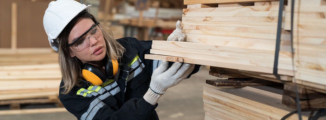 Holztechnikerin überprüft Holz in einer Lagerhalle.