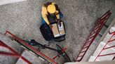 Postbotin sortiert Pakete im Rucksack und kniet dabei im Treppenhaus