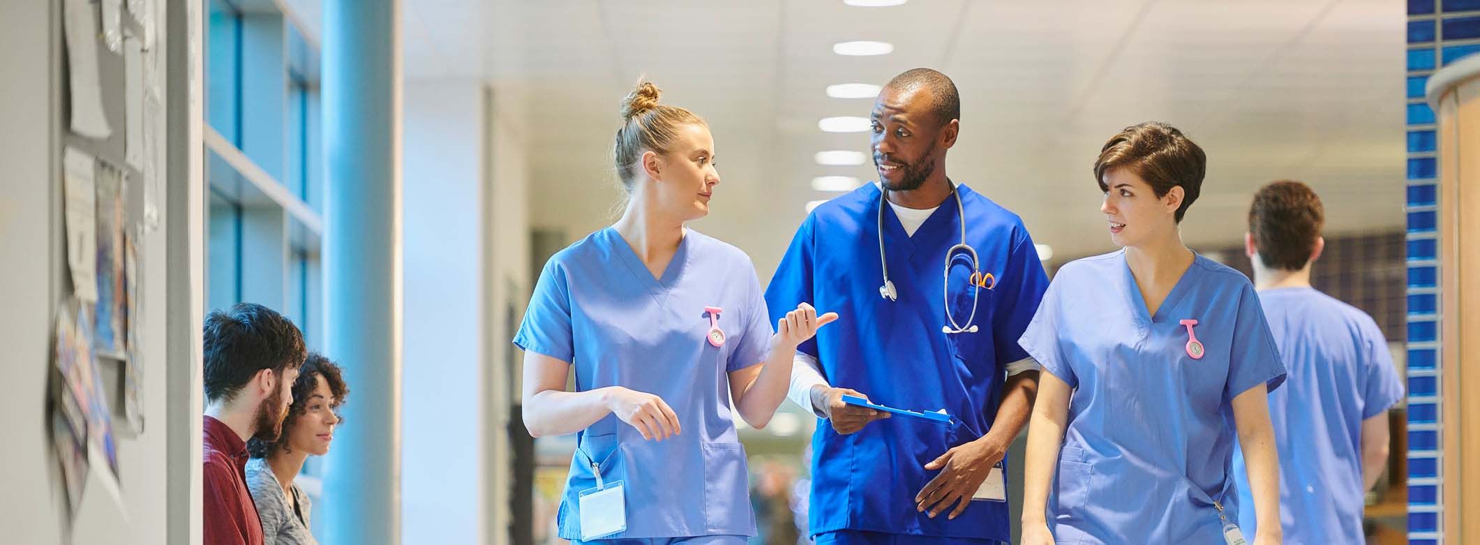 Gesundhets- und Krankenpflegehelfer gehen durch Krankenhausflur und unterhalten sich