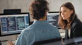 Zwei junge Mathematisch-technische Softwareentwickler sitzen vor Computern mit Codes und schauen sich an.