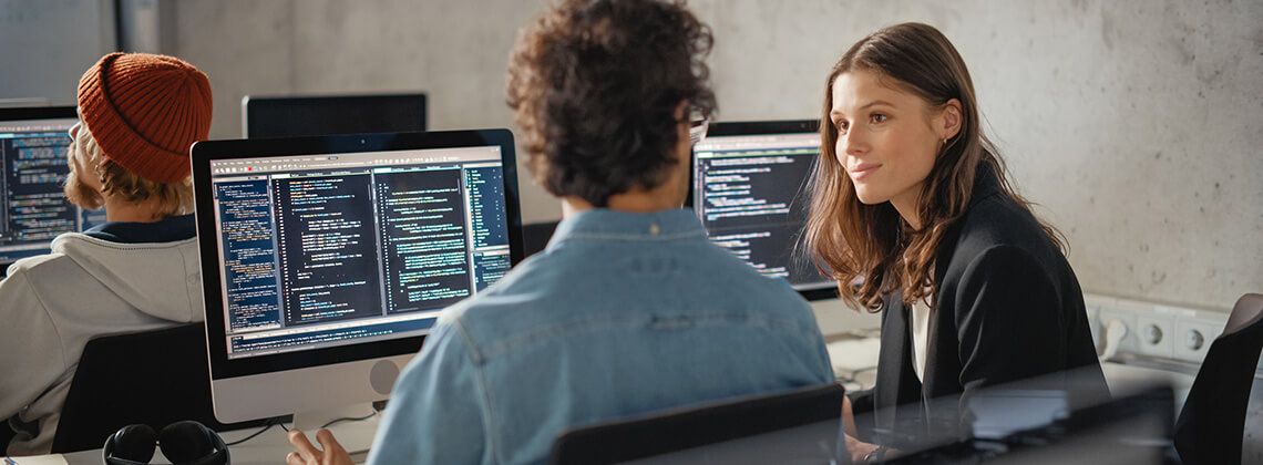 Zwei junge Mathematisch-technische Softwareentwickler sitzen vor Computern mit Codes und schauen sich an.