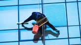 Gebäudereiniger putzt Fenster eines großen Gebäudes von außen