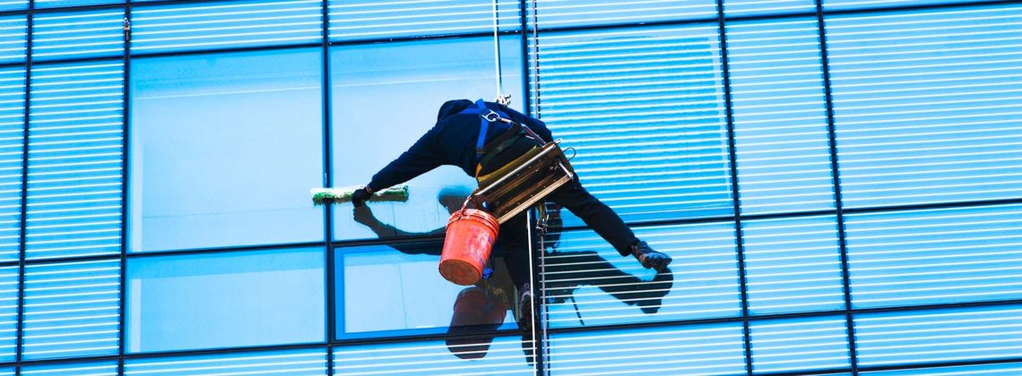 Gebäudereiniger putzt Fenster eines großen Gebäudes von außen