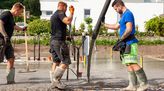 Mehrere Stahlbetonbauer stehen auf einer Baustelle und gießen ein Betonfundament.
