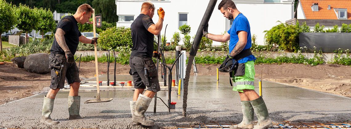 Mehrere Stahlbetonbauer stehen auf einer Baustelle und gießen ein Betonfundament.